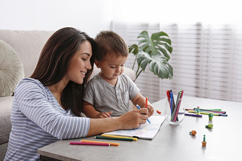 Young beautiful woman teaching her two year old son to draw at home. Woman spending quality time with her toddler child. Close up, copy space, background.