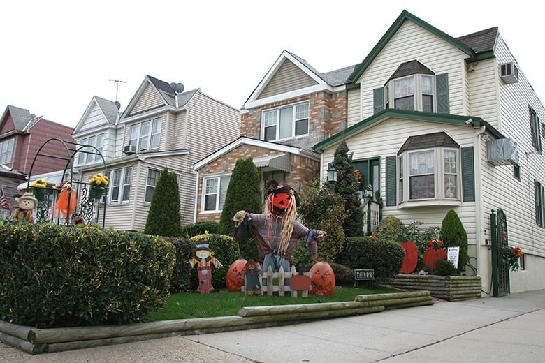 A scarecrow with a pumpkin beside him in a garden in front of house