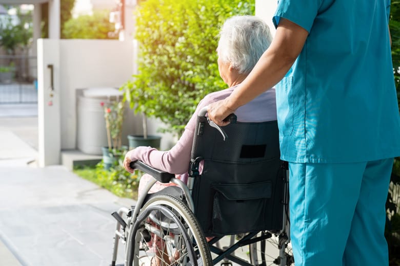 assisted-living-woman-being-pushed-in-wheelchair-outside-by-staff