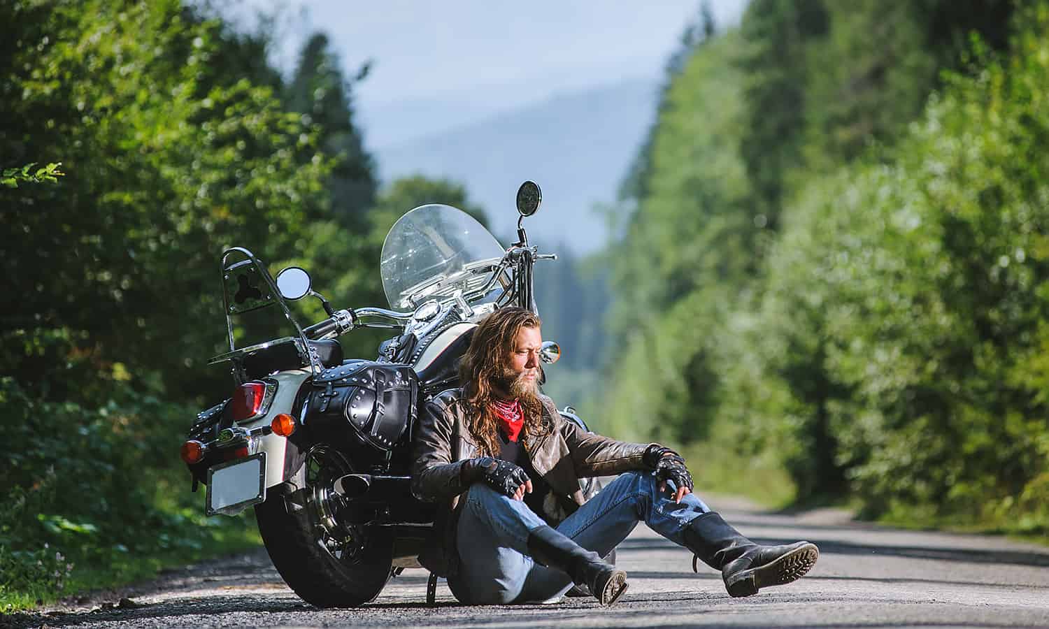 Motorcyclist sitting down on the road against his bike